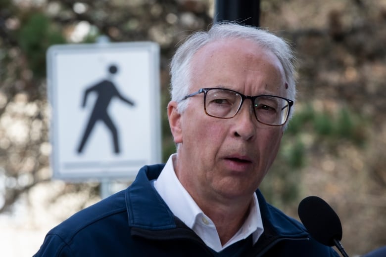 A man speaks into a mic outdoors, with a pedestrian walking sign behind him.