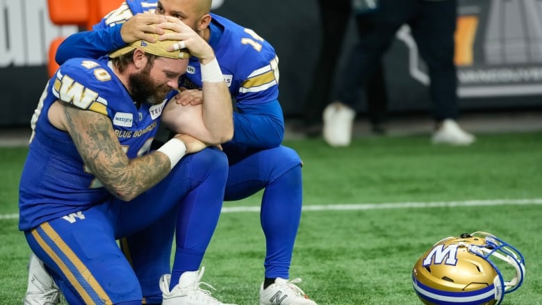 Two football players commiserate on the sidelines after a loss.