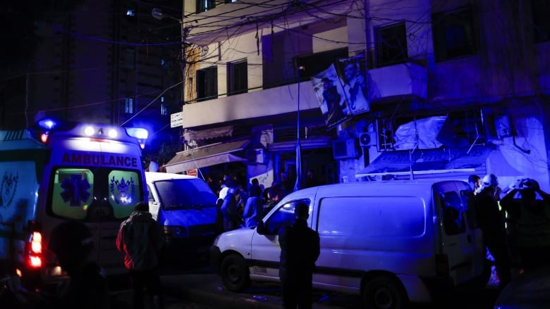 People stand outside of damaged building next to ambulances.