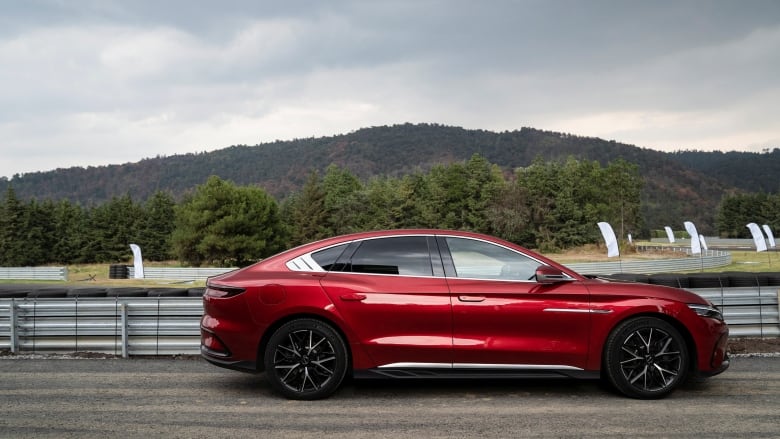 A red car is shown on a road outdoors.