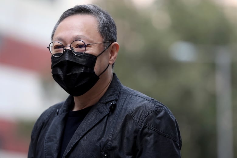 A man with glasses wears a black surgical mask over his nose and mouth. 