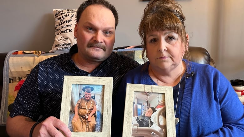 A man and a woman are shown holding photos of their daughter sitting on a couch.