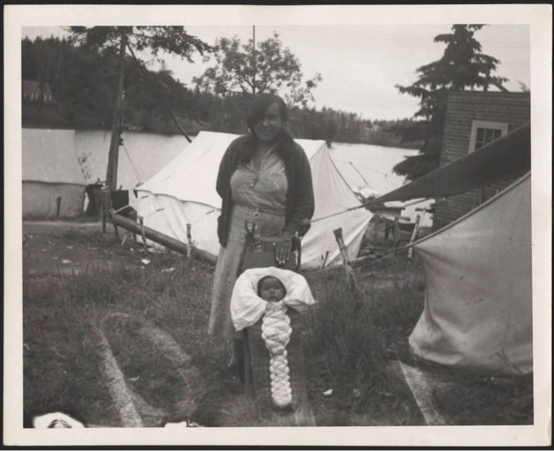 A black and white photo of a person and a baby outside.