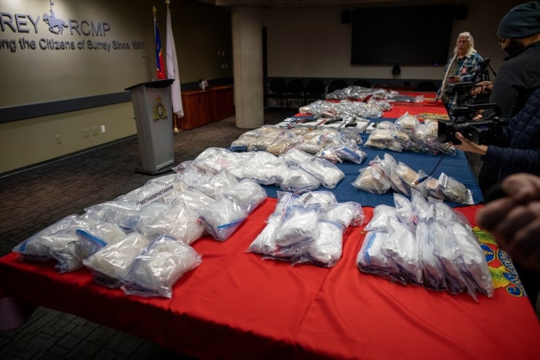 A table full of ziploc bags with various powders inside them, with camerapersons taking shots of them.