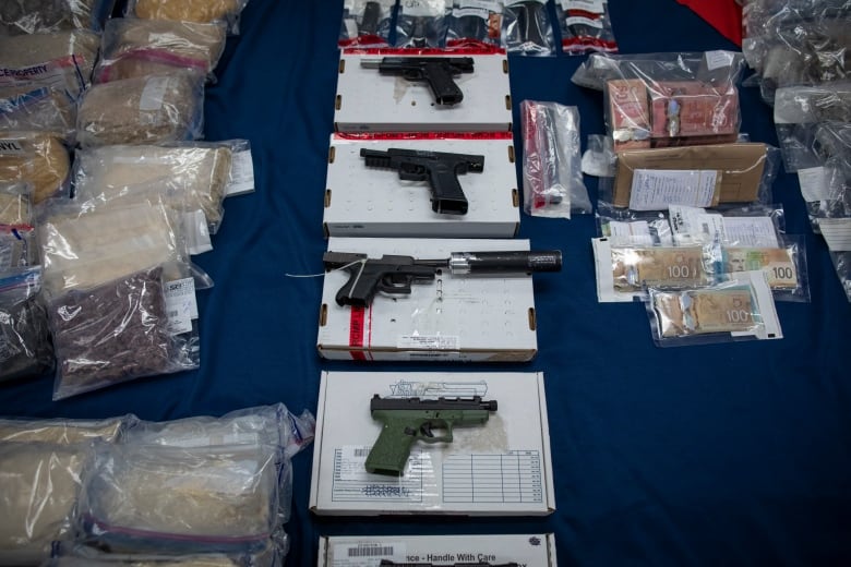 A table full of guns, bank notes and ziploc bags with powder inside.