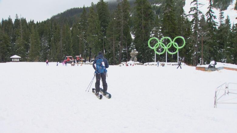 A person skis in front of the Olympic rings in a large area.