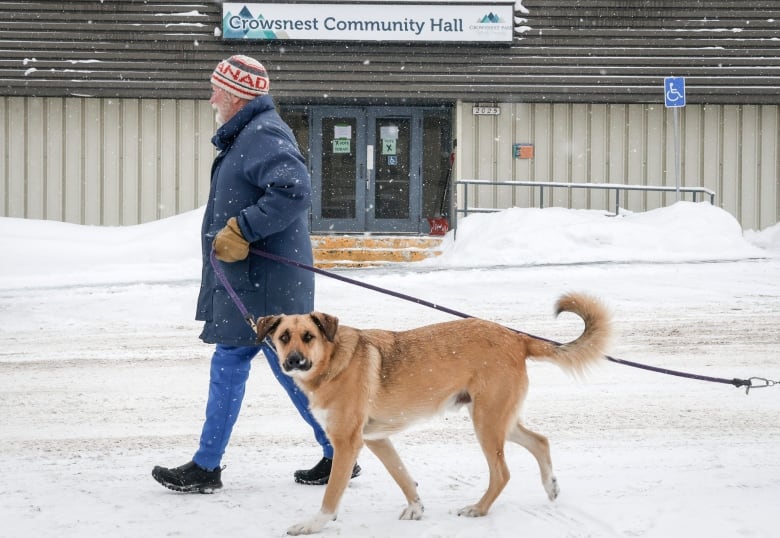 As snow falls around them, people enter a community hall.