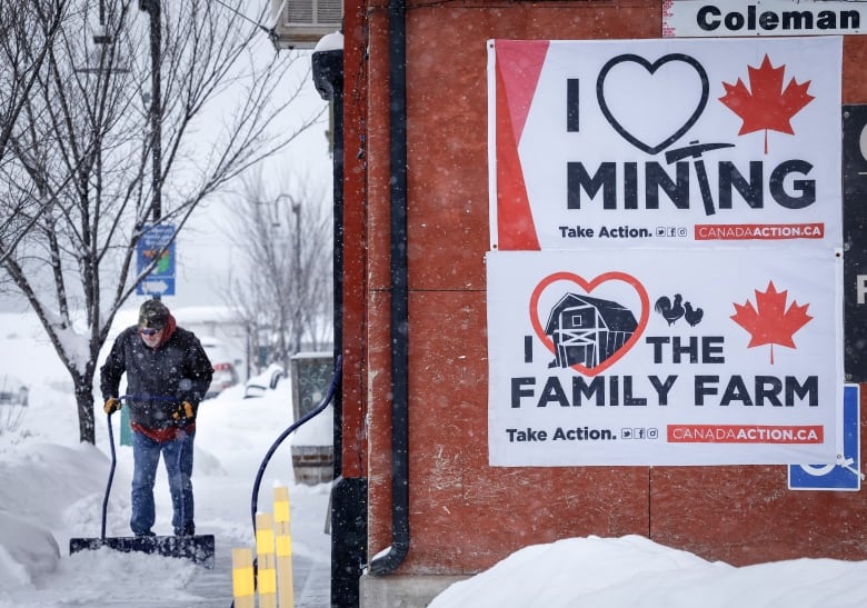 A man shovels snow next to signs supporting coal mining.